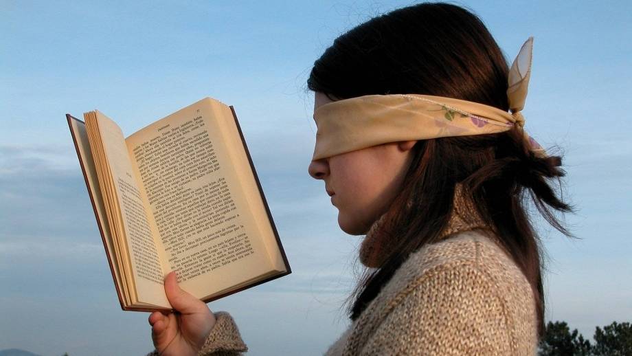Geblinddoekte vrouw met open boek in hand.