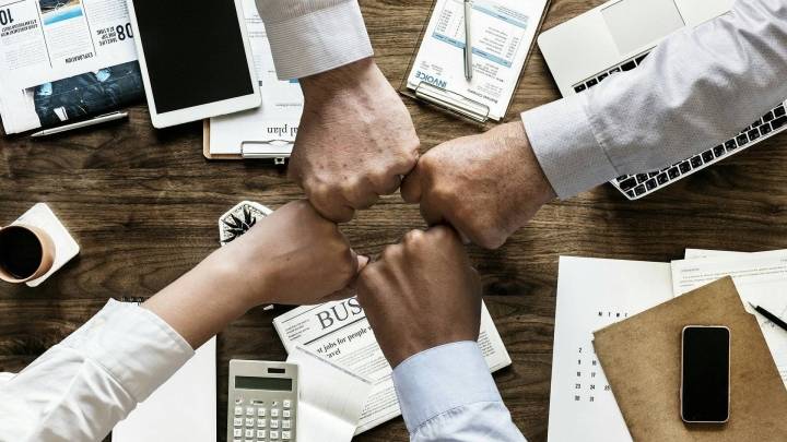Vier vuisten tegen elkaar boven een bureau vol schrijfmaterialen en rekenmachines.